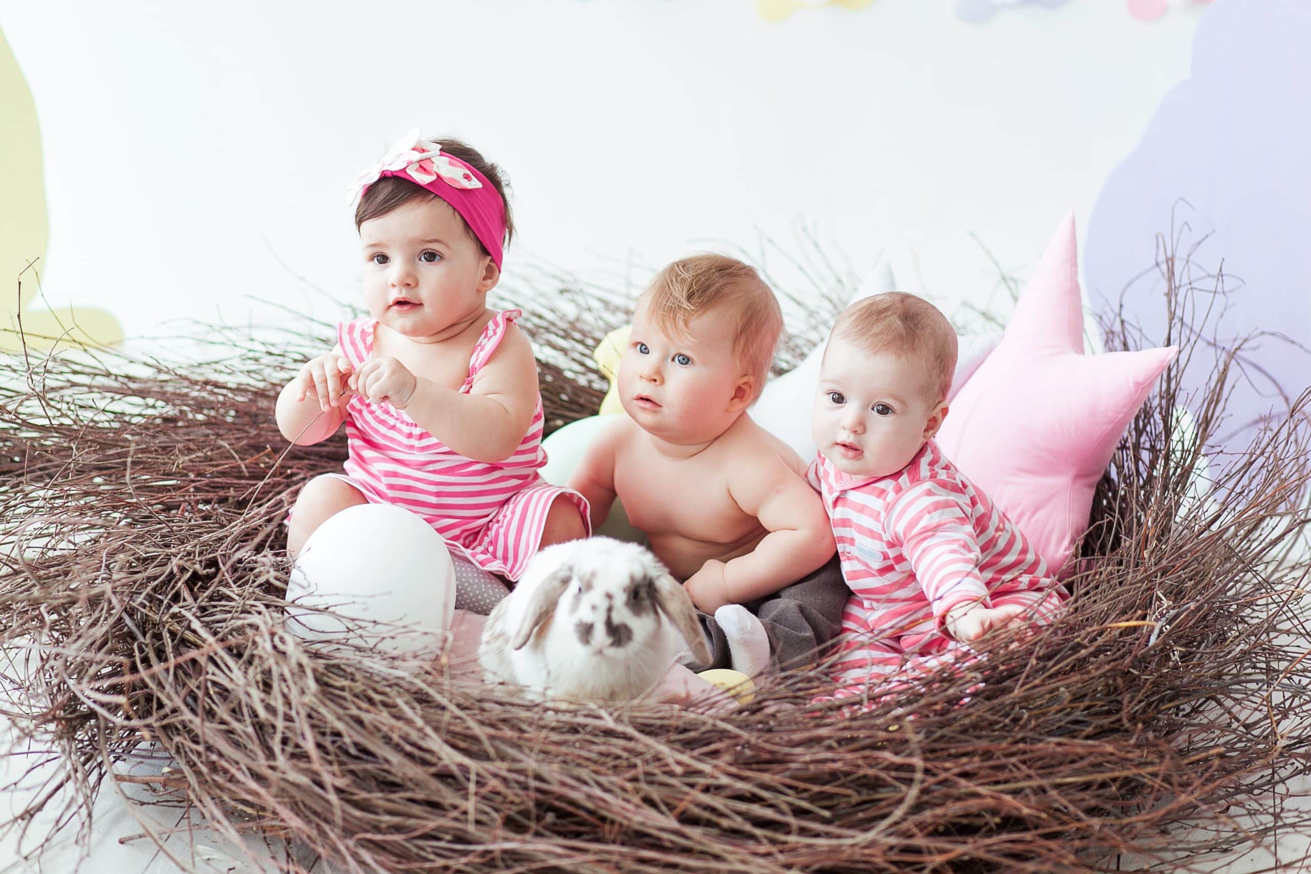Three cute little babies and rabbit with Easter eggs sitting in huge nest.